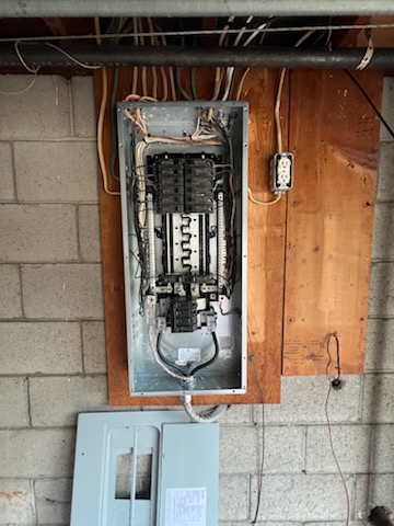 A replacement breaker panel installed on a basement wall of an older home, old cover removed